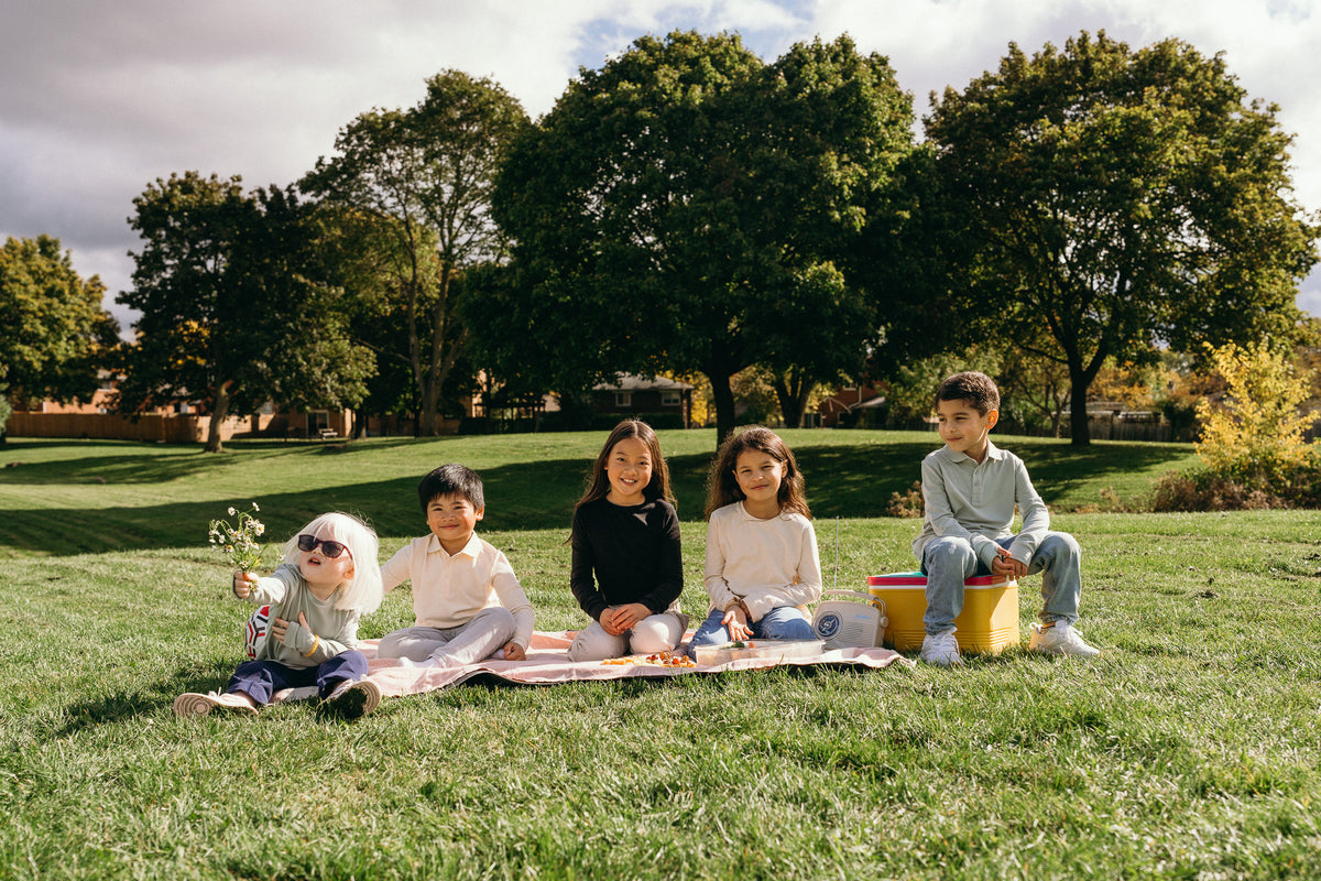 Five kids having a picnic in a sunny park wearing Ember & Ray UPF 50+ clothing