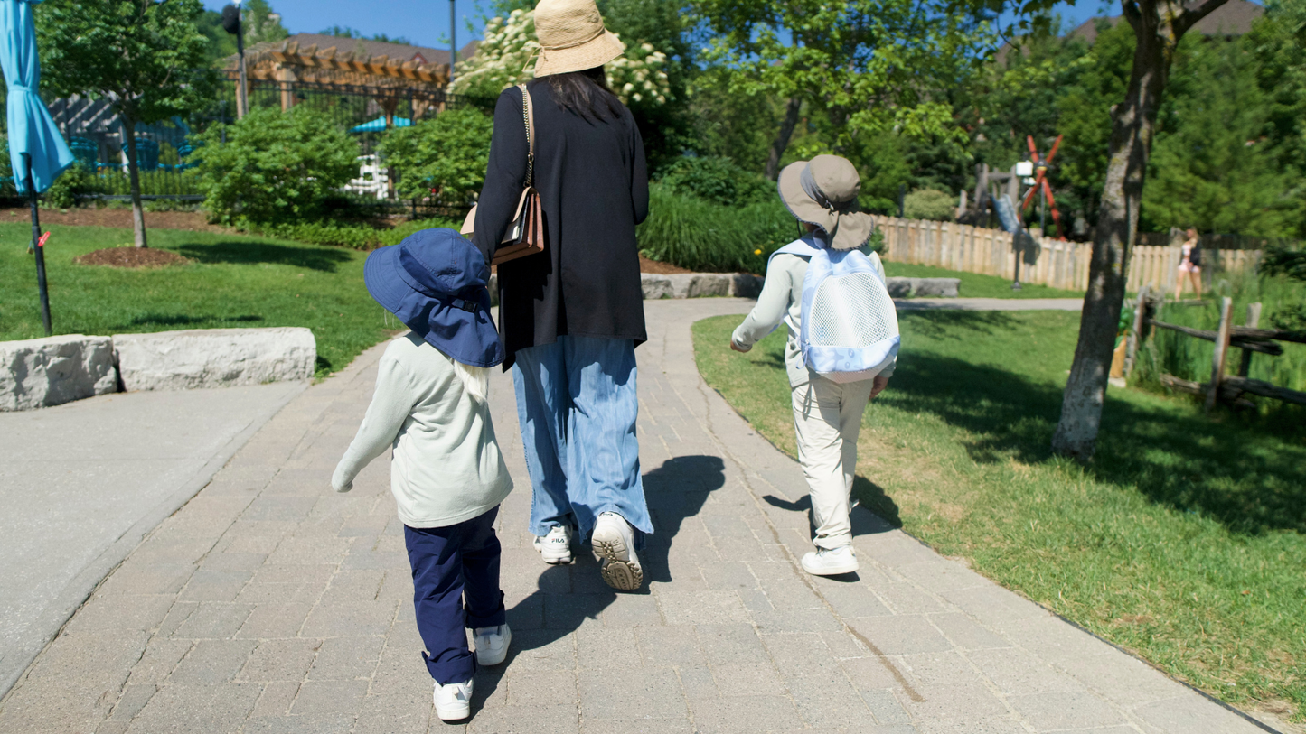 Parent walking outdoors with two children wearing Ember & Ray UPF 50+ clothing, sun hats, long sleeves, and pants for everyday sun protection.