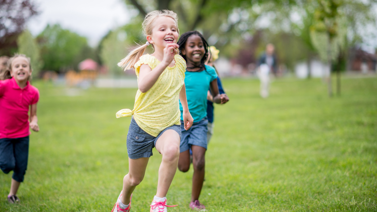 Children running outdoors on a grassy field during a sunny sports and active play day.