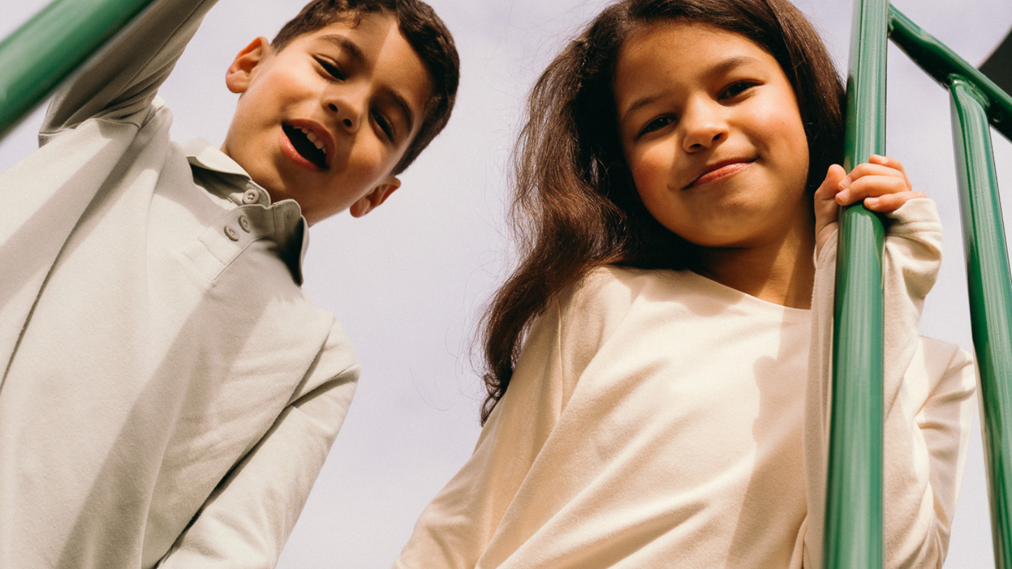Two kids wearing lightweight UPF 50+ clothing at a playground on a sunny day