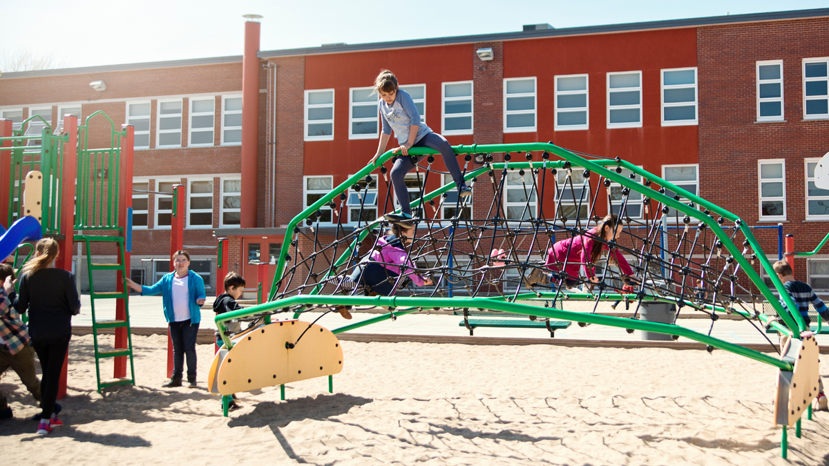 Children playing outdoors during school recess on playground equipment at an elementary school.