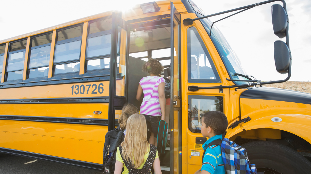 children wearing comfortable clothing and backpacks while going on a school bus on an outdoor school field trip.